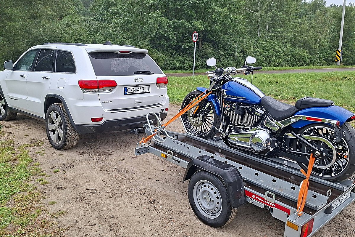 Motocykl przypięty pasami na przyczepie motocyklowej za samochodem terenowym